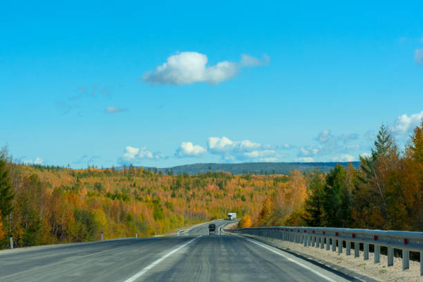 Bright autumn scene with road among orange and green trees and blue sky. Soft selective focus. Beauty of nature, travel concept.