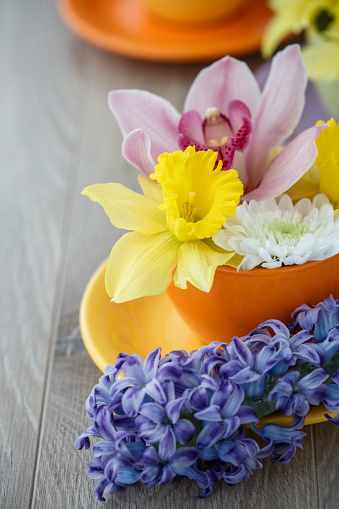 Close up shot of a small arrangement of different colorful spring flowers in a tea cup set up on a wooden table as a decoration.