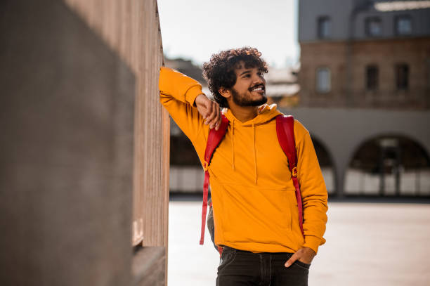 Dark-haired young guy in orange hoodie with a backpack