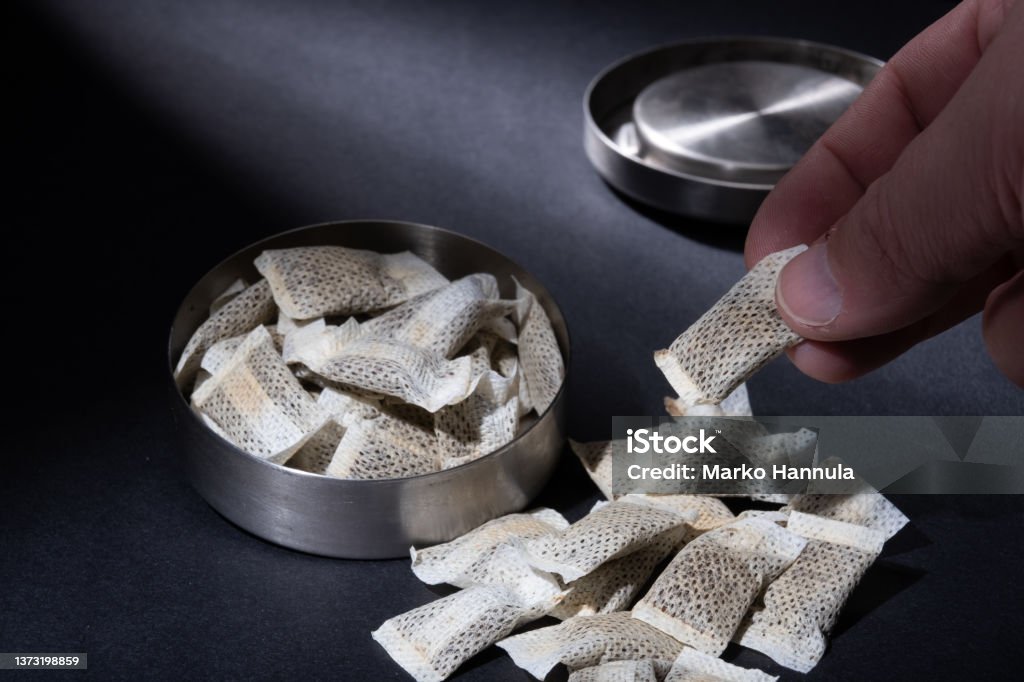 Closeup of metallic Swedish snus can with white portions of smokeless tobacco pouches against a dark background. Helsinki / Finland - FEBRUARY 28, 2022: Closeup of metallic Swedish snus can with white portions of smokeless tobacco pouches against a dark background. Chewing Tobacco Stock Photo