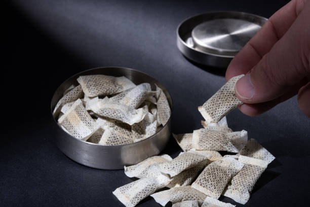 Closeup of metallic Swedish snus can with white portions of smokeless tobacco pouches against a dark background. stock photo