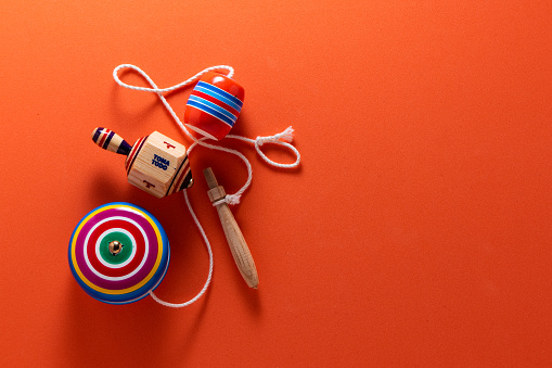 Photograph of Mexican wooden toys, a yoyo, a balero, and a spinner, all on a bright orange background.