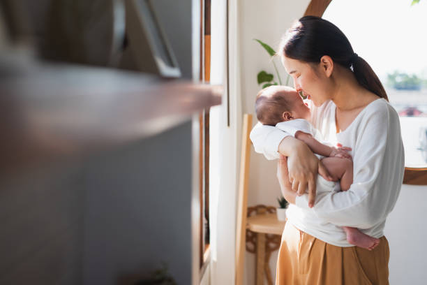 Young Asian mother holding her newborn baby in bedroom stock photo