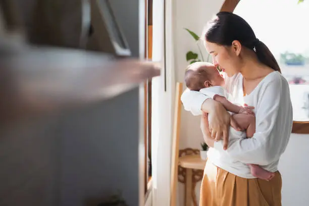 Photo of Young Asian mother holding her newborn baby in bedroom