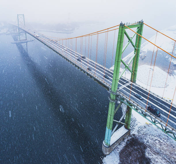 An aerial drone view of a suspension bridge during a snowstorm.