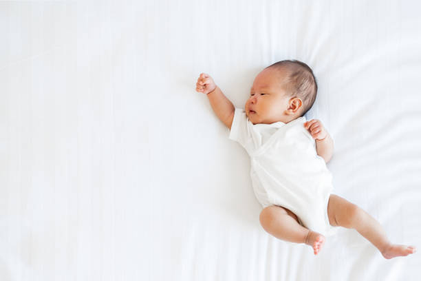 Portrait of Asian newborn baby in white cloth on bed funny pos stock photo