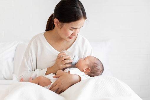 Mother breast feeding milk to Asian newborn baby on white bed