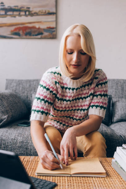 istock Beautiful Blond Female Student Taking Notes while Reading on her Tablet in the Living Room 1373215510