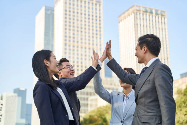 asian businesspeople celebrating success with high-fives stock photo