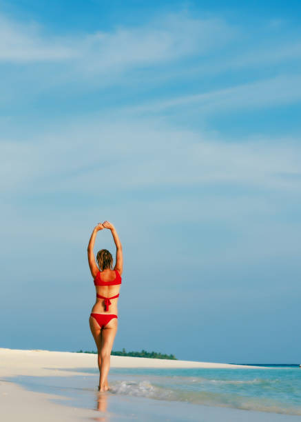 Girl at seaside wearing biking holding inflatable mattress. View from behind of a young woman alone on the beach looking at the sea on a sunny day. Beautiful travel summer picture