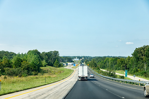 Expressway traffic heading down a steep hill toward a highway roadside truck stop and traveler rest area with a blue \