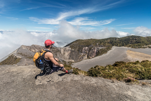 tourist with backpack sitting watching the main crater in the Irazu Volcano National Park in Costa Rica