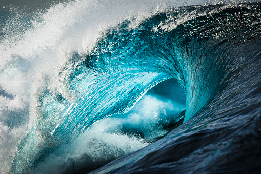 Close up detail of powerful teal blue wave breaking in open ocean on a bright sunny afternoon