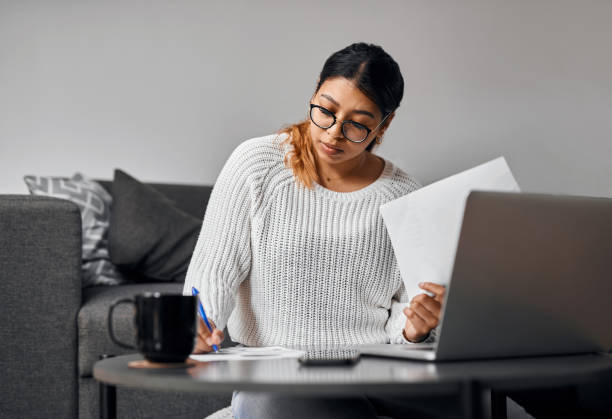 istock Shot of a young woman using a laptop and going through paperwork at home 1373236113