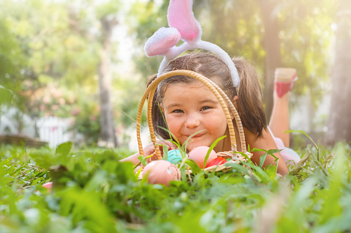 Portrait of happy child in bunny ears and easter basket in backyard