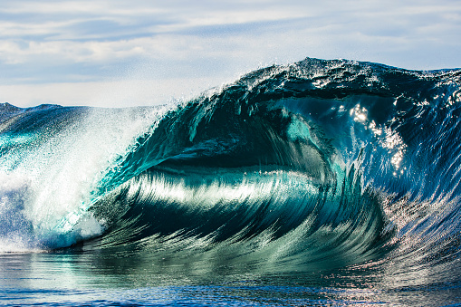 Perfect and powerful teal blue wave breaking in open ocean on a bright sunny afternoon