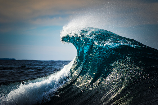 Cresting teal blue wave breaking in open ocean
