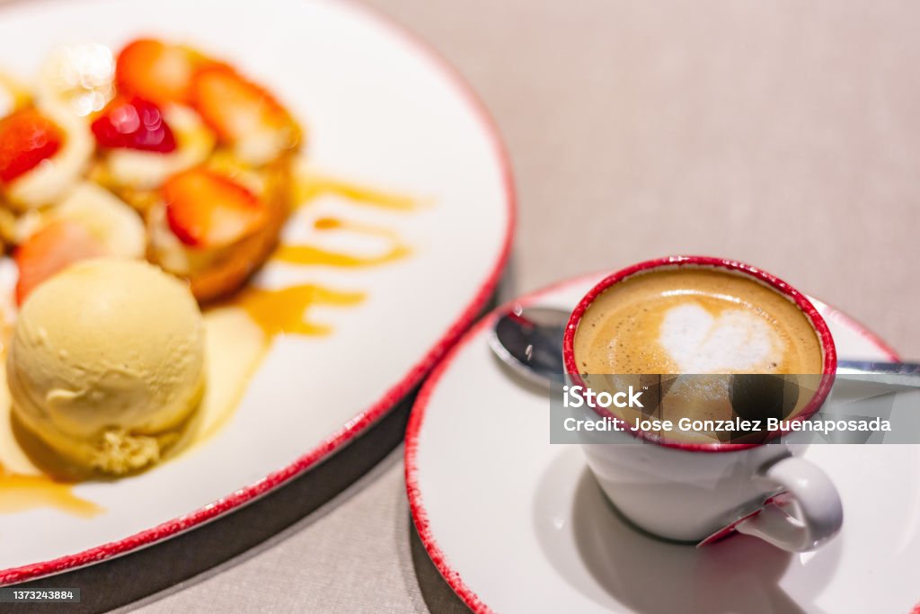 Cup of foamy coffee and dessert with croissant, banana, strawberries and ice cream. Delicious and appetizing Madrid, spain February 13 2022. Cup of foamy coffee and dessert with croissant, banana, strawberries and ice cream. Delicious and appetizing Coffee - Drink Stock Photo