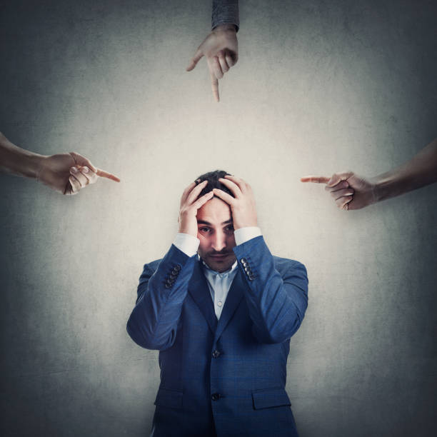 istock Ashamed and desperate businessman covers head with hands, as multiple persons pointing fingers towards him, blaming and scolding. Man suffering emotional breakdown and depression, being under pressure 1373244340