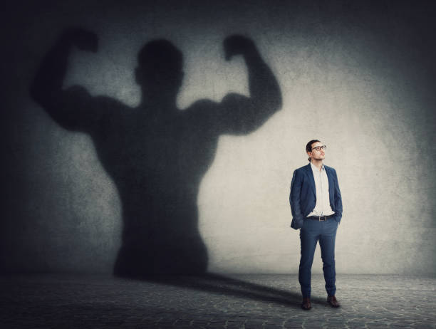 istock Confident businessman keeps hands in his pockets while casts a powerful person shadow on the wall behind. Business person transformation as metaphor for leadership and motivation 1373244357