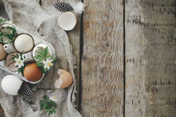 Easter rustic flat lay. Natural easter eggs, blooming spring flowers, feathers, burlap on rural wooden table. Happy Easter! Simple stylish festive decoration on table. Flat lay with space for text