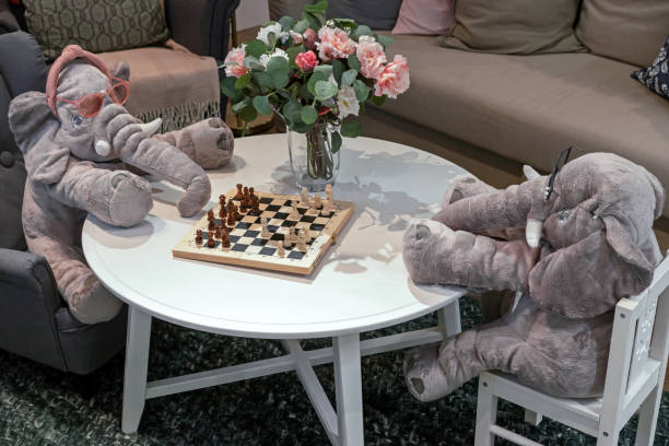 istock Two plush elephants in glasses play chess at a white table. 1373246128