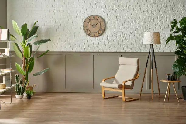 Photo of Room wall concept, brick and classic style, clock armchair lamp and green plant botanic interior decor, brown parquet and carpet.