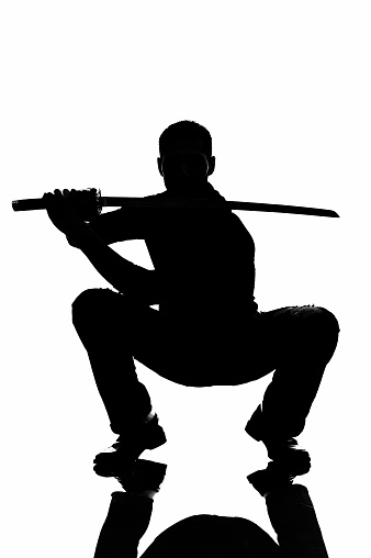 Male squatting in casual clothing with katana in hand.