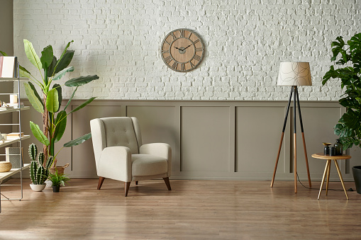 Room wall concept, brick and classic style, clock armchair lamp and green plant botanic interior decor, brown parquet and carpet.