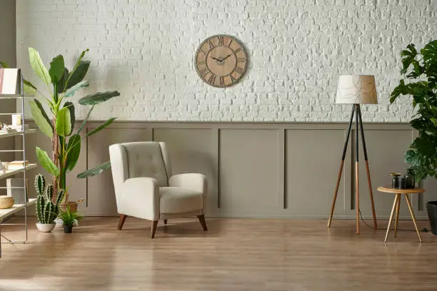 Photo of Room wall concept, brick and classic style, clock armchair lamp and green plant botanic interior decor, brown parquet and carpet.