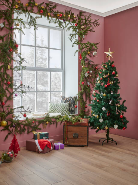istock Christmas tree and yellow fireplace in front of the decorative windows, interior room, pine branch decoration, gift box and furniture chair and sofa design. 1373249578