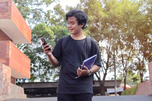 istock cheerful Asian student holding a notebook and mobile phone 1373250659