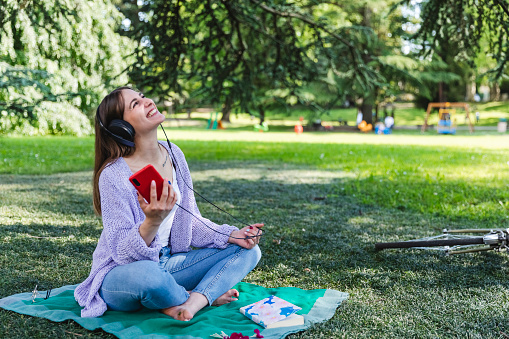 Happy woman listening music with smartphone sitting at the park