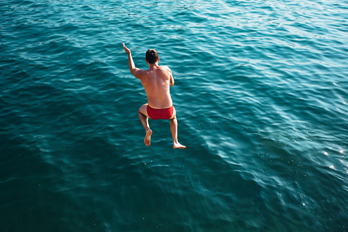 Man jumping off cliff into the sea. Summer fun lifestyle.