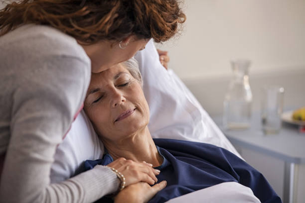 Woman kissing her mother at hospital Close up of lovely daughter visiting and kissing sick mother on forehead while resting in hospital bed. Senior patient laying on gurney with eyes closed while daughter assuring a speedy recovery. Old mom patient being kissed while recovering from disease in nursing home. sick woman hospital bed stock pictures, royalty-free photos & images
