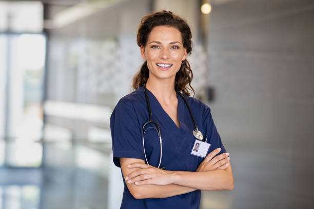 Happy nurse at hospital Portrait of happy young female nurse with folded arms standing in hospital hallway. Confident doctor woman in uniform and stethoscope looking at camera with copy space. Portrait of beautiful young healthcare worker working in private clinic. female doctor stock pictures, royalty-free photos & images