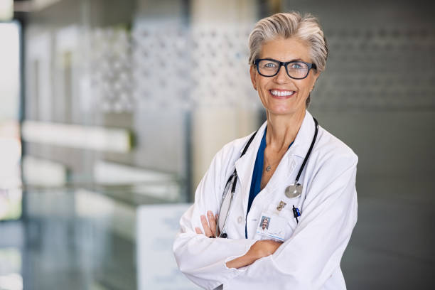 Successful senior doctor smiling Portrait of proud female doctor with stethoscope around neck at medical clinic. Happy smiling senior woman doctor at hospital lobby looking at camera with copy space. Mature general practitioner or physician feeling confident. female doctor stock pictures, royalty-free photos & images