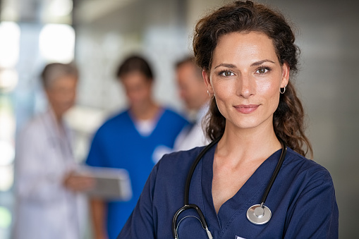 Portrait of proud female nurse with stethoscope around neck at medical clinic. Happy smiling young woman doctor at hospital lobby with copy space. Medical staff feeling confident after a major operation and looking at camera.