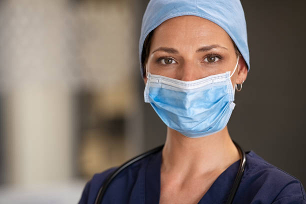 Proud nurse wearing surgical mask at hospital Portrait of young woman doctor wearing face mask and scrubs at hospital. Confident medical practitioner with surgical mask looking at camera. Determined female doctor in hospital hallway with copy space during covid-19 pandemic. female nurse stock pictures, royalty-free photos & images