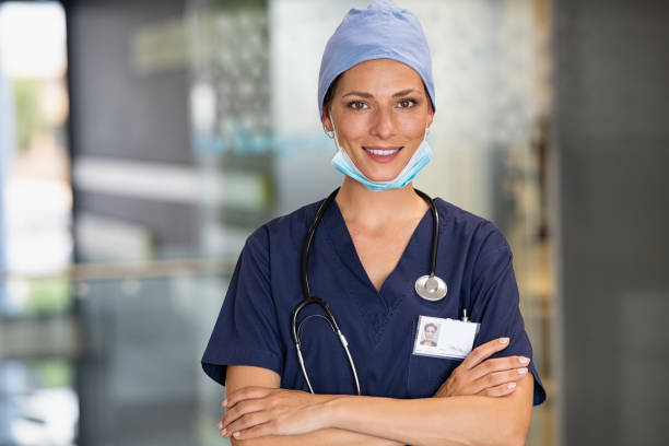 Satisfied female surgeon at hospital Portrait of  successfurl young woman doctor wearing face mask and scrubs in hospital. Confident and reliable medical practitioner with surgical mask looking at camera. Smiling nurse standing in clinic hallway with crossed arms and copy space. anaesthetist stock pictures, royalty-free photos & images