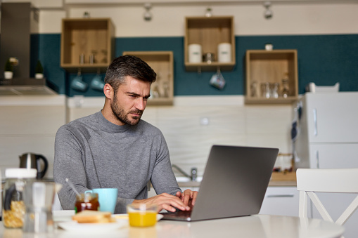 Portrait of a young man using a laptop while having breakfast at home