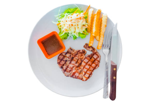 Top view of pork steak served with crisp golden french fries and fresh salad accompanied by BBQ or tomato sauce in white plate isolated on white background. Cut Out