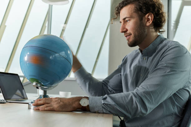 The world is his playground! Smiling businessman spinning the globe while working in the office. spinning photos stock pictures, royalty-free photos & images
