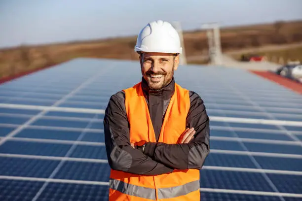 A handyman standing on the rooftop with solar panels and smiling at the camera.