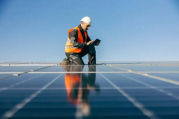 A worker kneeling on the roof and checking on solar panels.