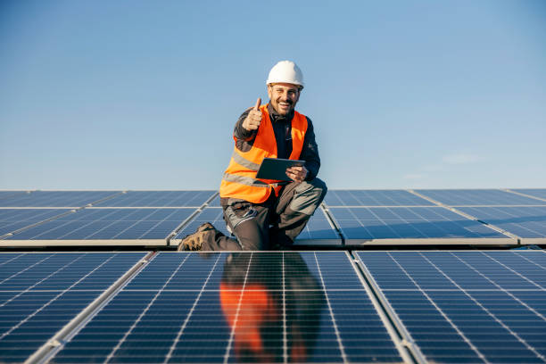 A handyman on roof surrounded by solar panels giving thumbs up for eco living. stock photo