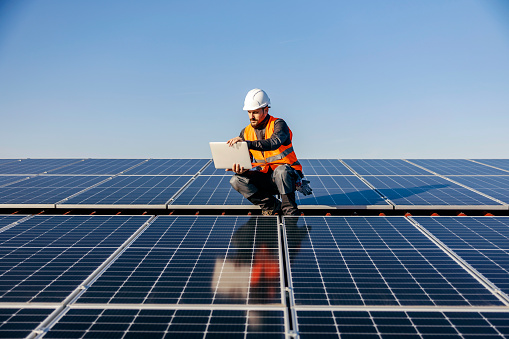 Un trabajador en el techo usando una computadora portátil cargada por la energía solar. photo