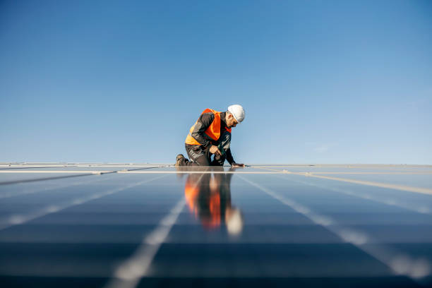 Worker kneeling and sets solar panel. A handyman on the rooftop installing solar panels. rooftop solar stock pictures, royalty-free photos & images