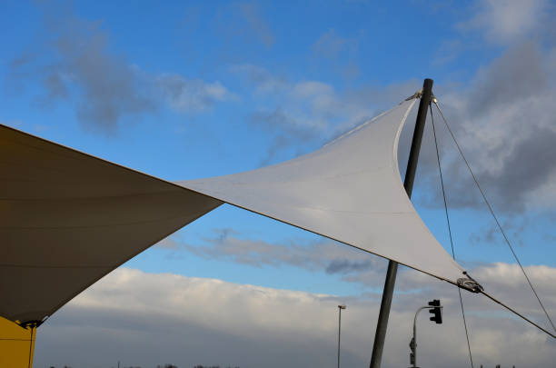 telone bianco teso, ombreggiato dal sole e dalla pioggia sulla terrazza del ristorante, sul parco giochi dell'asilo, sulla piattaforma. solo un albero e corde tese attaccate saldamente alle estremità - beach rope nautical vessel harbor foto e immagini stock