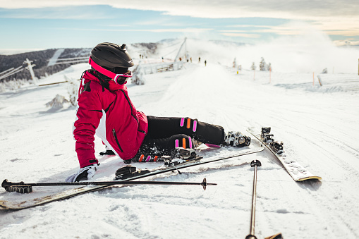 A young girl skier in a ski suit after falling on a mountain slope. The concept of winter sports.